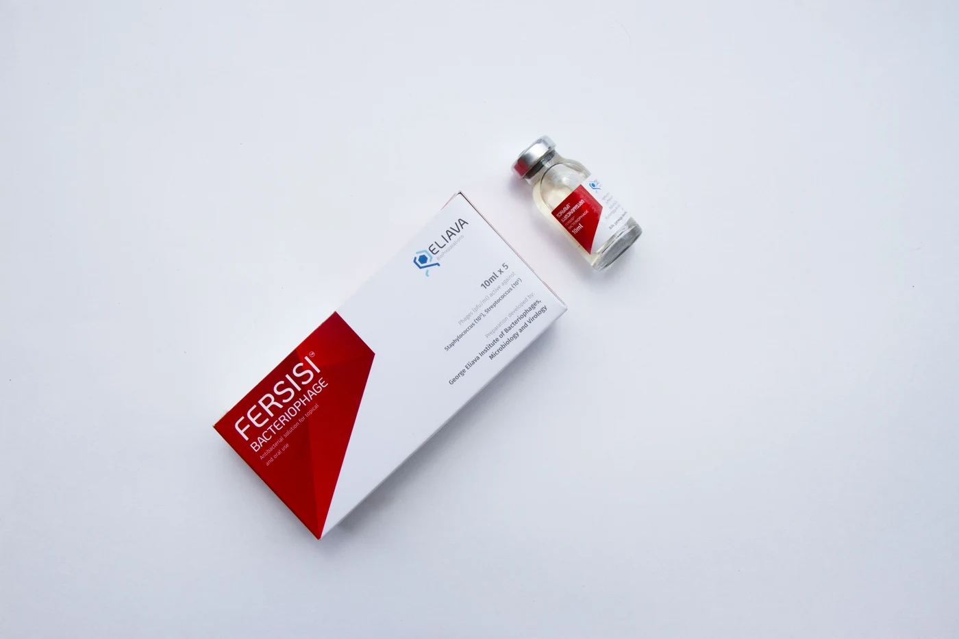 A medicine vial with a wraparound label beside its carton on a neutral background